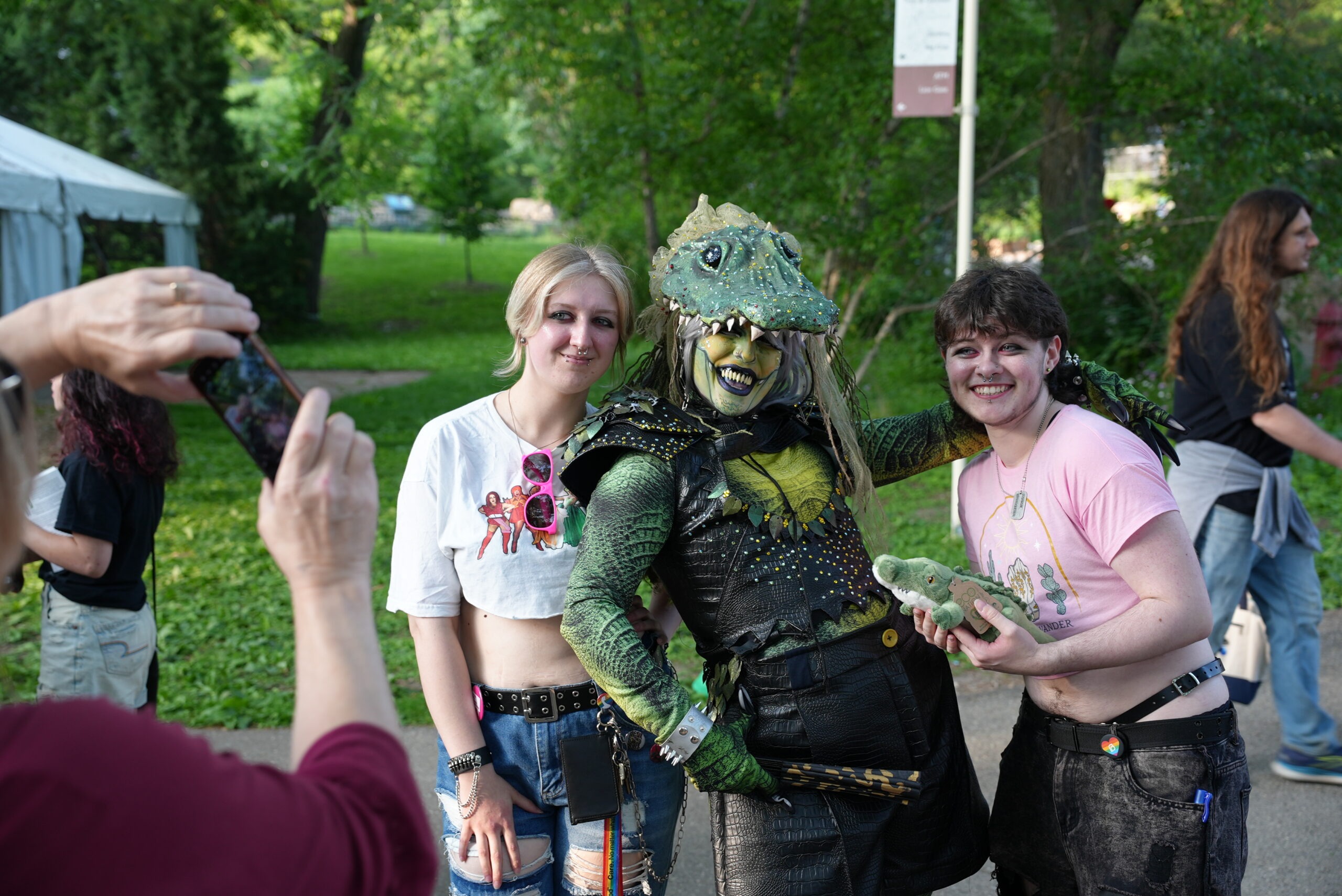 Two guests posing for a photo with a drag queen in an alligator costume